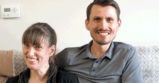 Sarah and Eric smiling at the camera while sitting on a couch.