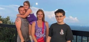 A family of four poses for a photo with a scenic sky in the background.
