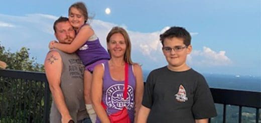 A family of four poses for a photo with a scenic sky in the background.
