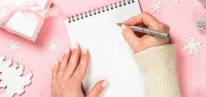 Hands writing on a blank notepad surrounded by festive decorations.