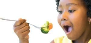 Child eating broccoli and carrots on a fork