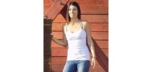 Rachel Hurtado wearing a white tank top and jeans standing by a wooden structure.