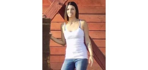 Rachel Hurtado wearing a white tank top and jeans standing by a wooden structure.