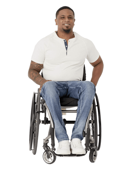 A man in a wheelchair smiles at the camera, wearing a white polo shirt and blue jeans.