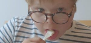 Child in striped shirt and glasses eats food from a fork.