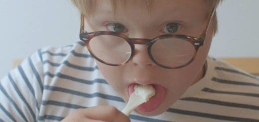 Child in striped shirt and glasses eats food from a fork.