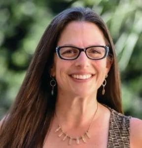 Emily Berman smiling wearing glasses and a necklace.