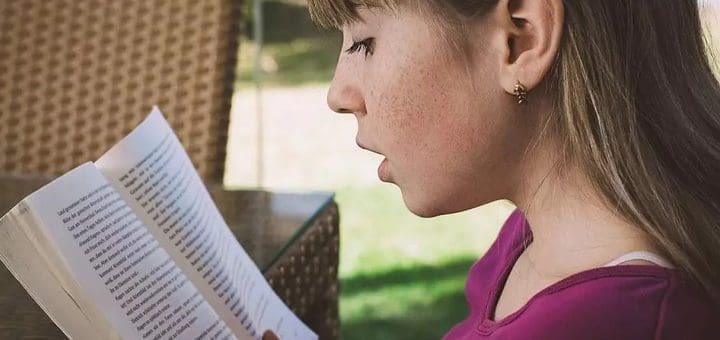 Young person reading a book outdoors.