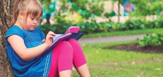Young girl in blue shirt and pink leggings using a tablet in a park.
