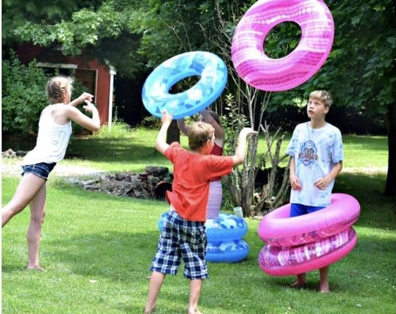 Three children play in a grassy yard with colorful inflatable rings.
