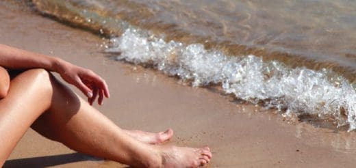 Woman's legs on a sandy beach with a gentle wave washing ashore.
