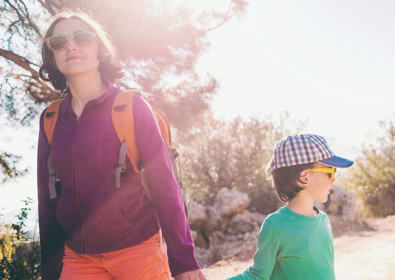 A woman and a child walk outdoors on a sunny day, both wearing sunglasses.