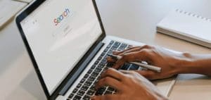 Person's hands typing on a laptop with the word "Search" on the screen