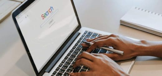 Person's hands typing on a laptop with the word "Search" on the screen