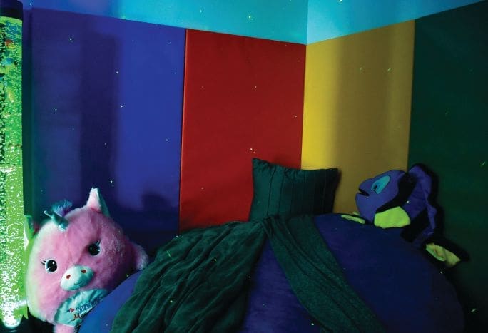 A calming closet with colorful walls, soft furnishings, and a bubble tube.