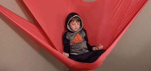 A child sits in a red sensory swing with their eyes closed.