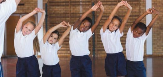 Children in gym class stretching with arms overhead