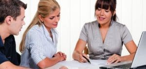 Three people sit at a table with papers and a laptop.