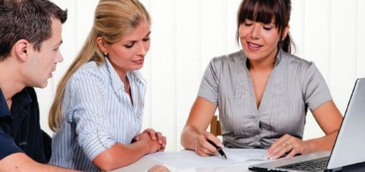 Three people sit at a table with papers and a laptop.