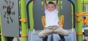 Child in white shirt and khaki pants hangs from playground equipment.