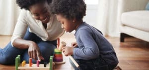 A mother and child play with a wooden toy on the floor.