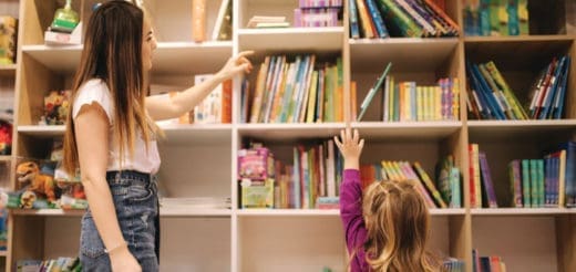 Woman and child reach for books on a shelf.
