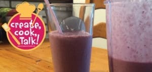 Glass filled with a purple fruit smoothie next to a blender pitcher.