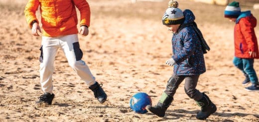 Children play soccer on a sandy field.