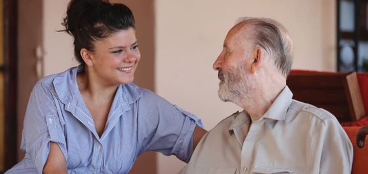 Young woman smiling while interacting with an elderly man, representing the caregiving responsibilities of the sandwich generation.