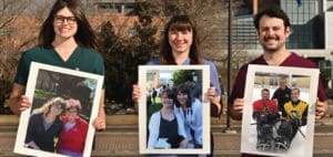 Three people holding framed photos of other people.