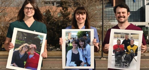 Three people holding framed photos of other people.