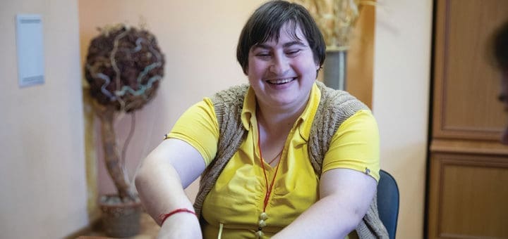 A woman smiles while wearing a yellow shirt and a brown vest.