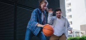 Two people play basketball outdoors in front of a building.
