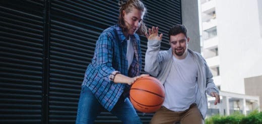 Two people play basketball outdoors in front of a building.