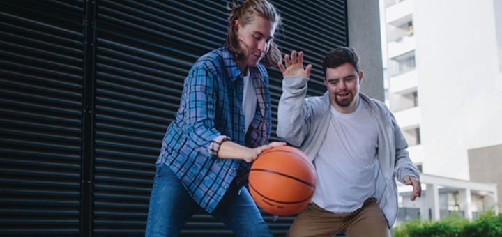 Two people play basketball outdoors in front of a building.
