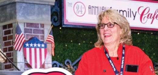 Woman in red jacket smiling with American flags and "Family Cafe" banner in background