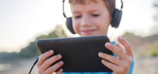 A young boy wearing headphones smiles while holding a tablet.