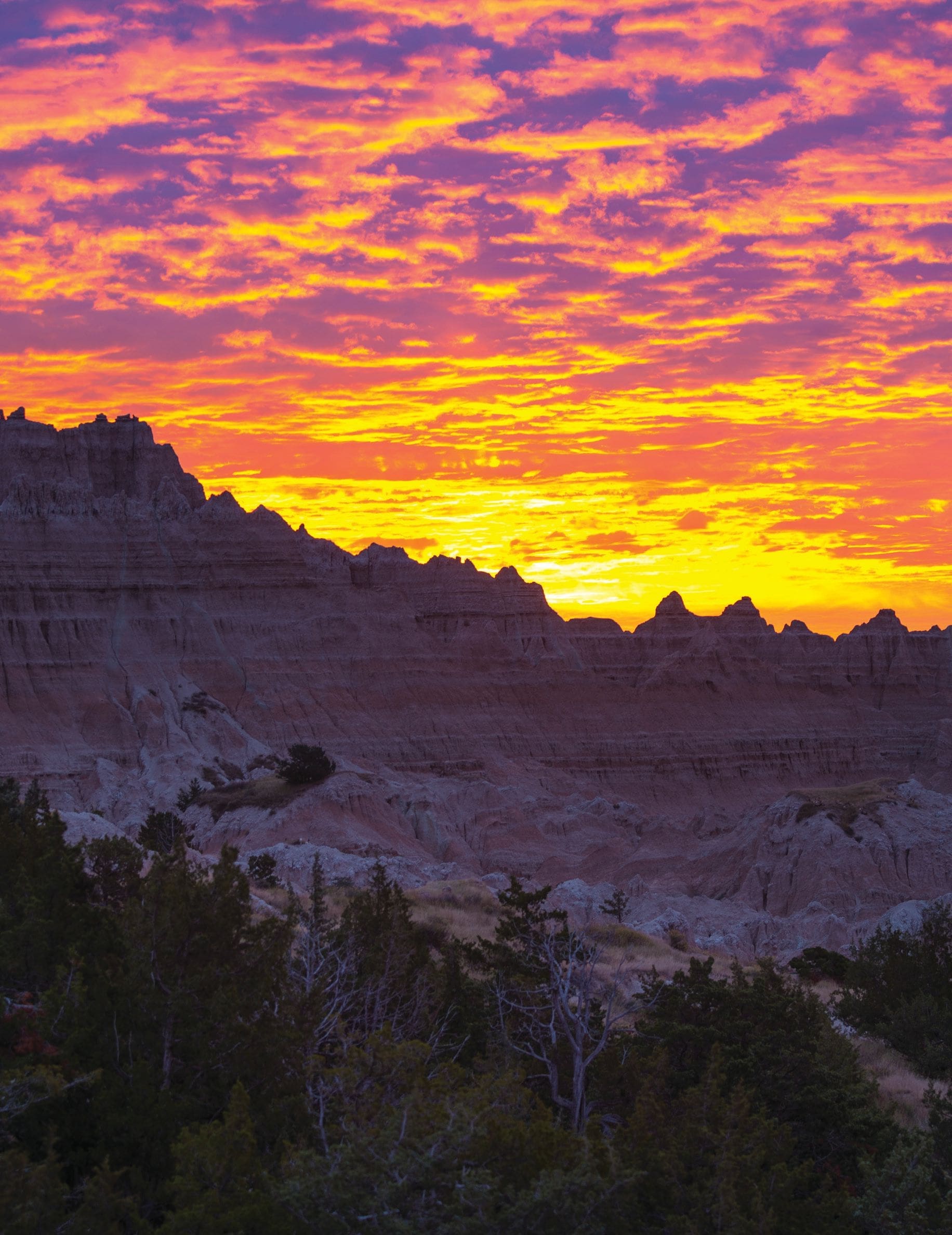 Pink and orange sunrise casting a warm glow over the rugged rock formations of Badlands National Park.