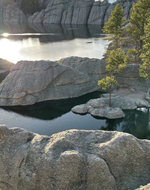 Serene lake reflecting rocky shore and pine trees at Custer State Park
