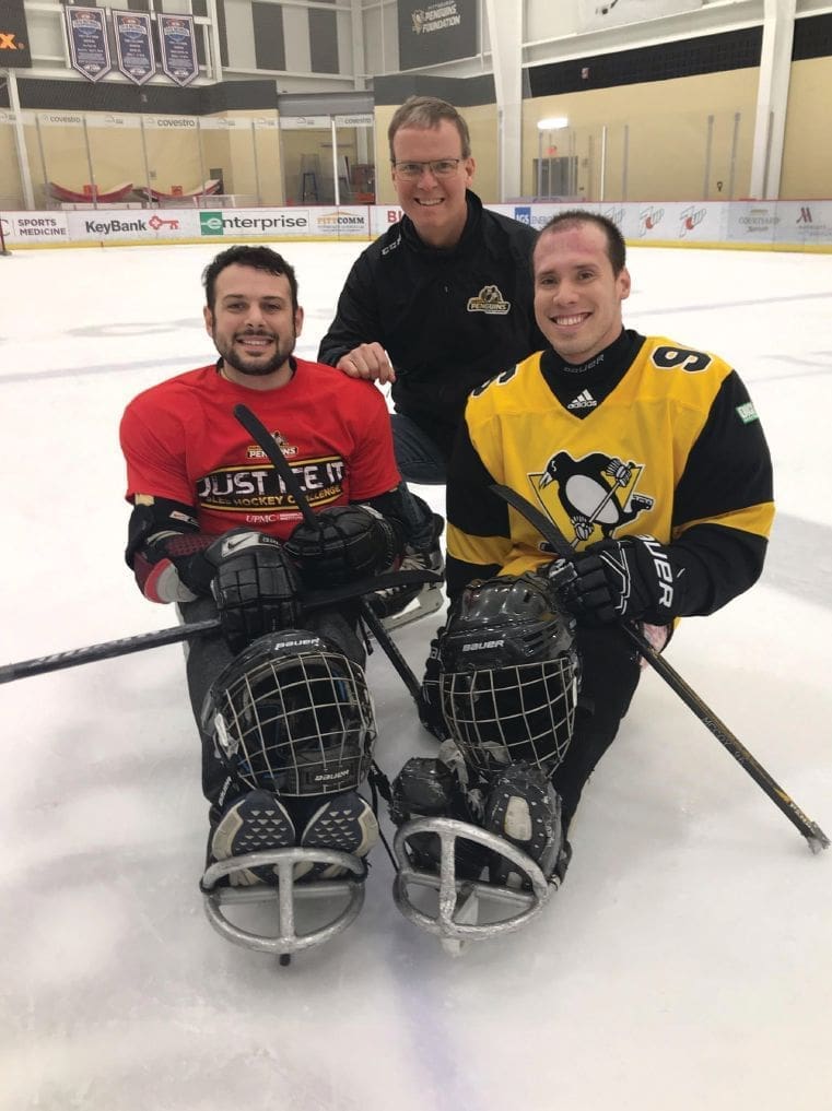 Dr. Andrew McCoy and two other men in hockey gear on an ice rink.