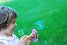 Child blowing bubbles with a bubble wand outdoors.