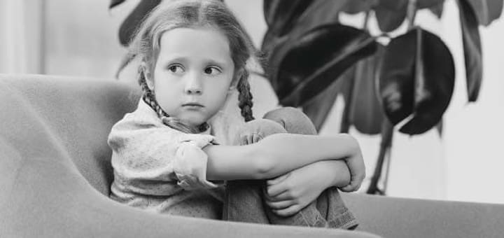 A young girl with braided hair sits curled up on a chair.
