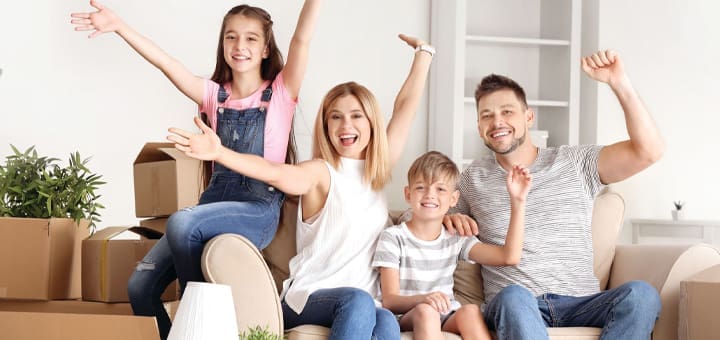 Family with arms raised in excitement surrounded by moving boxes.