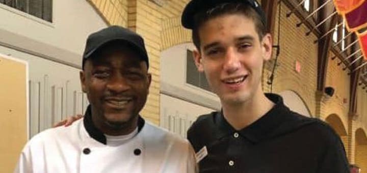 Two men, one in a chef's coat and the other in a polo shirt, smile at the camera.