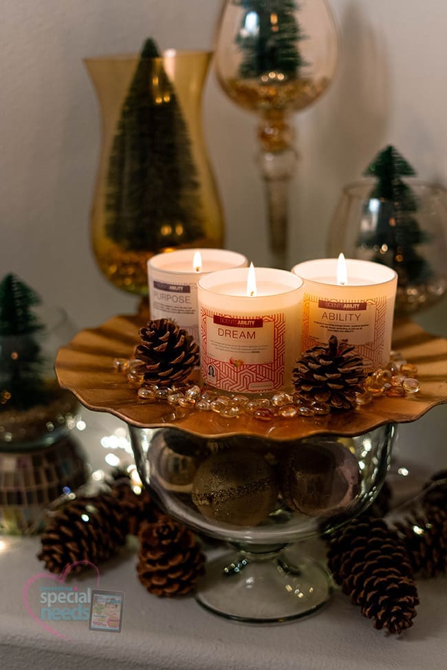 Three lit candles in glass jars with pinecones on a decorative stand.