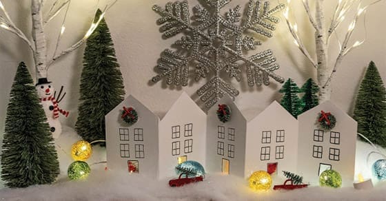 A miniature village of paper houses with Christmas trees and a snowman.