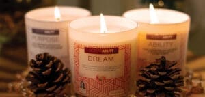 Three lit candles, labeled "Purpose," "Dream," and "Ability," sit in a decorative arrangement with pinecones.