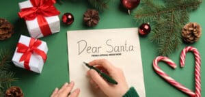 Hand writing "Dear Santa" on a letter surrounded by Christmas decorations.