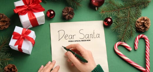 Hand writing "Dear Santa" on a letter surrounded by Christmas decorations.