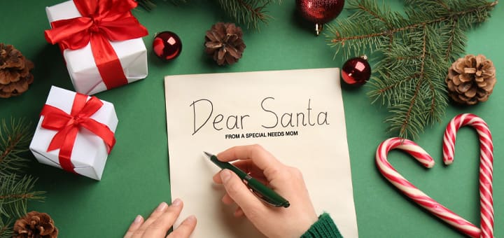Hand writing "Dear Santa" on a letter surrounded by Christmas decorations.